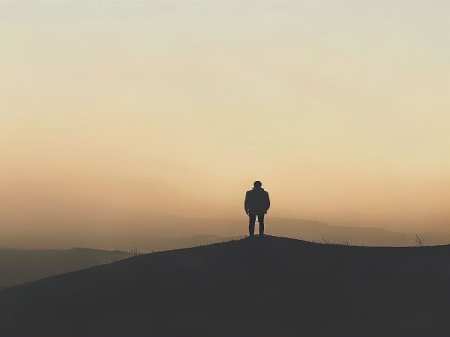 A silhouette of a person standing alone on a hill, looking out at a soft, hazy horizon, representing the weight of choos