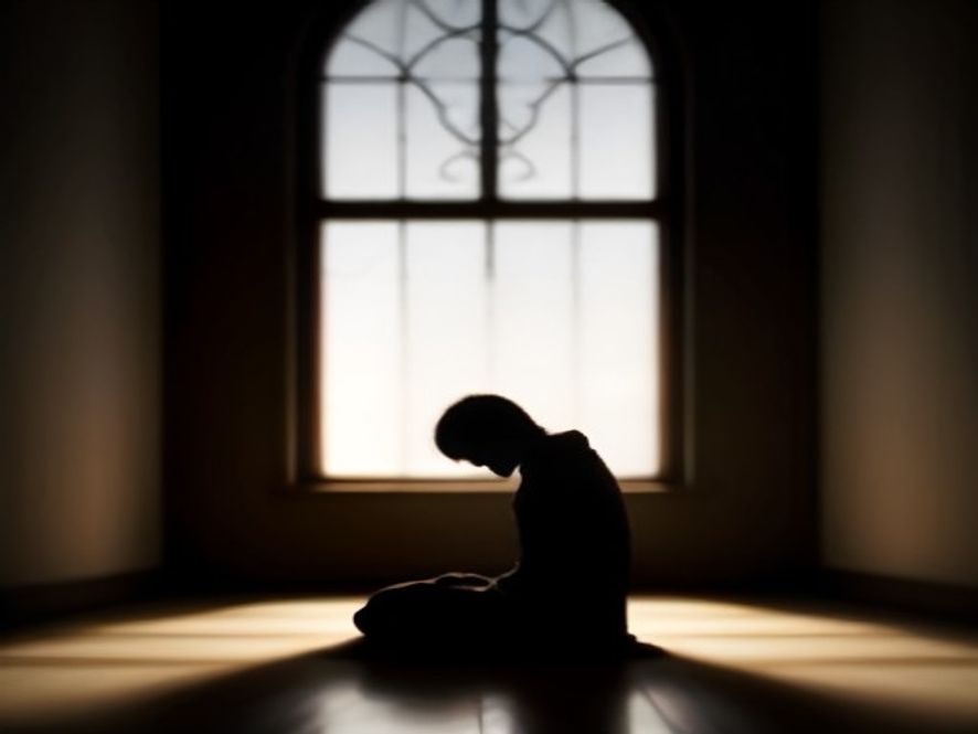 A silhouette of a person sitting alone in prayer, light streaming in from a nearby window, representing personal reflect