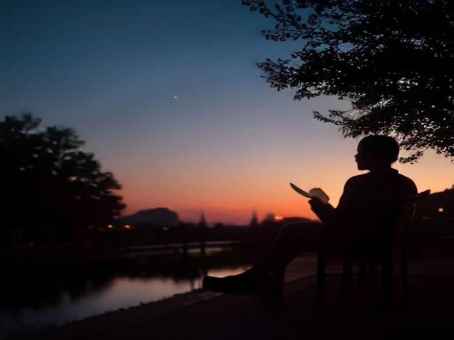 A person sitting on a porch at dusk, looking thoughtful and reflective, with the silhouette of a tree in the background.